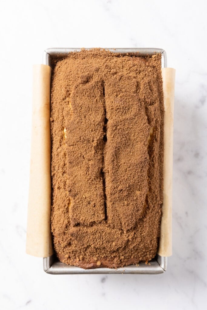 A coffee cake in a loaf pan sits on a marble surface shortly after baking.