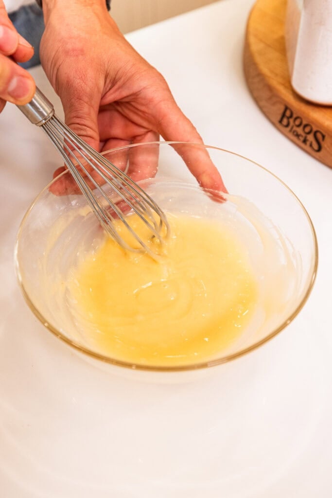 A hand whisking together ingredients to form a vanilla glaze.