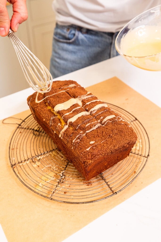 A whisk drizzling vanilla glaze over a coffee cake loaf.