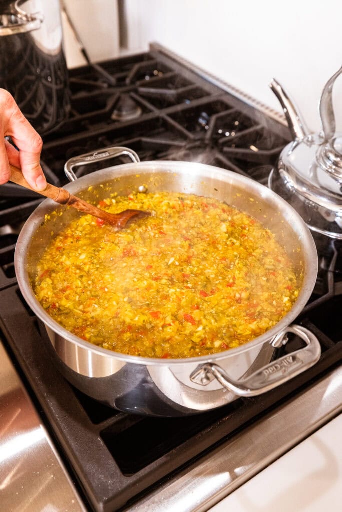 Pickle relish cooks in a pot on a stove.