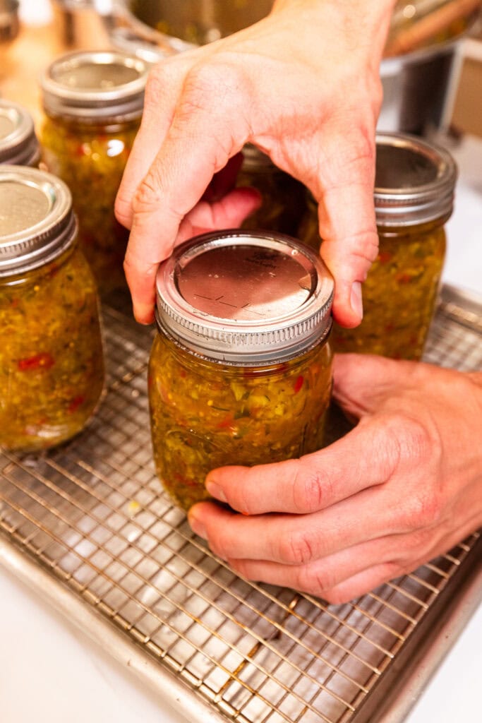 A hand tightens down a ring on top of a jar filled with pickle relish.