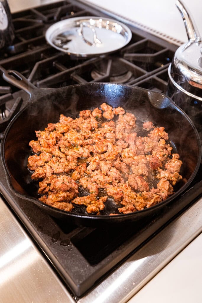 Sausage browns in a skillet on a stove.