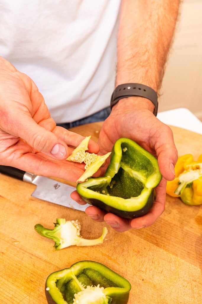 A hand removing the pith and seeds from a bell pepper with a knife.