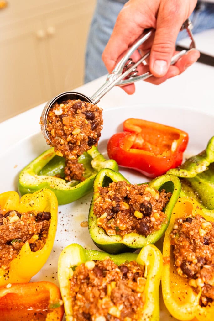 A hand scoops ground beef stuffing into a hollowed out bell pepper.