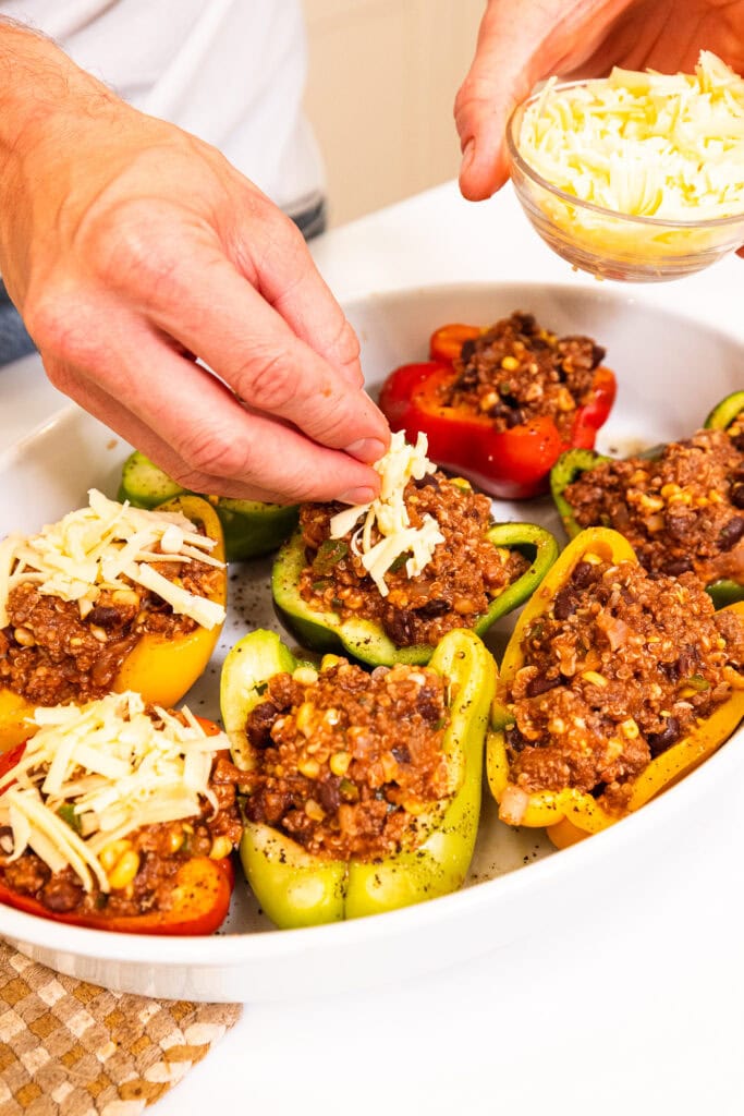 Shredded cheese getting sprinkled over stuffed bell peppers.