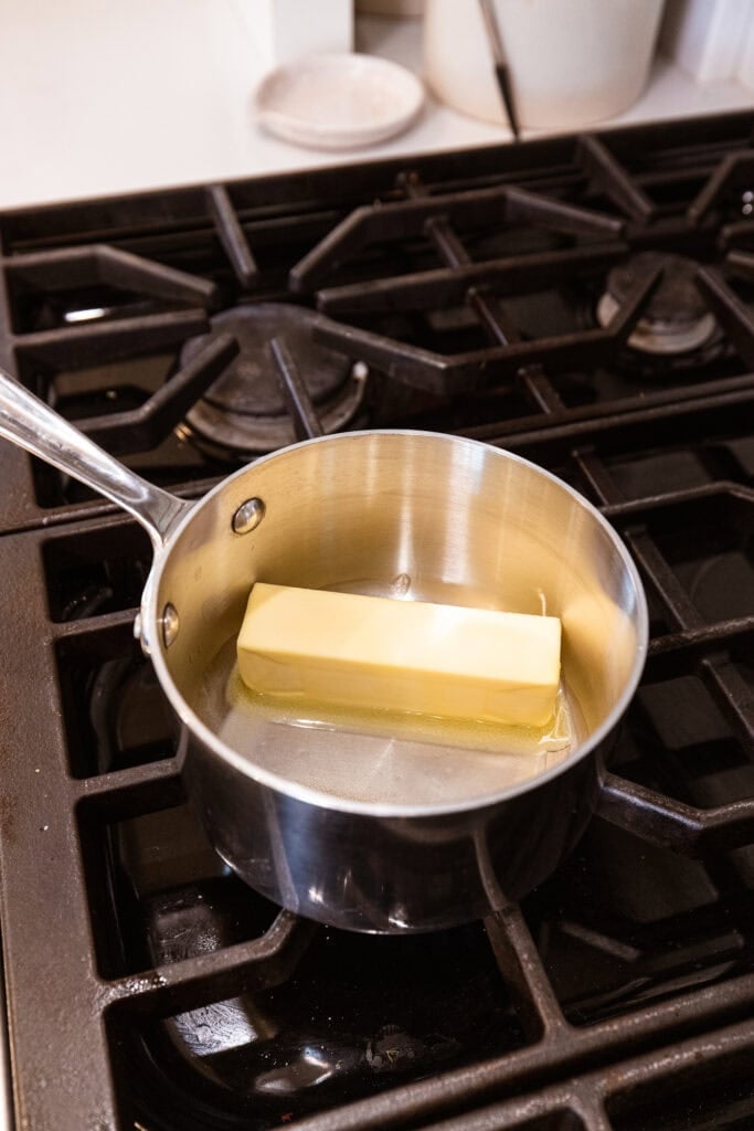 A stick of butter melts in a saucepan over a stove.