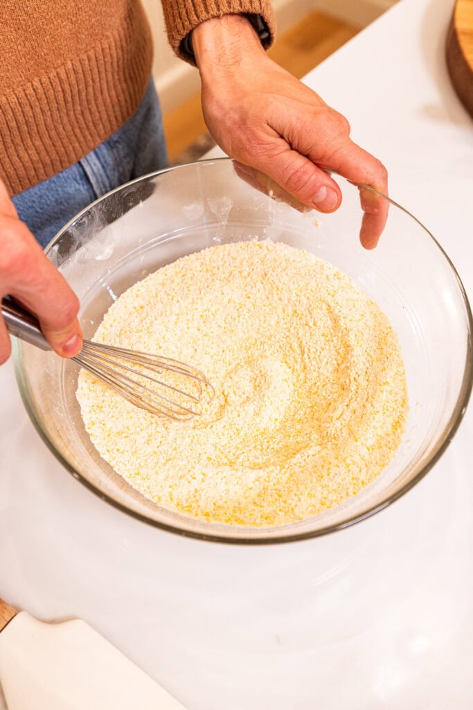 Cornmeal, flour, baking powder, and kosher salt get combined in a bowl to create a batter.