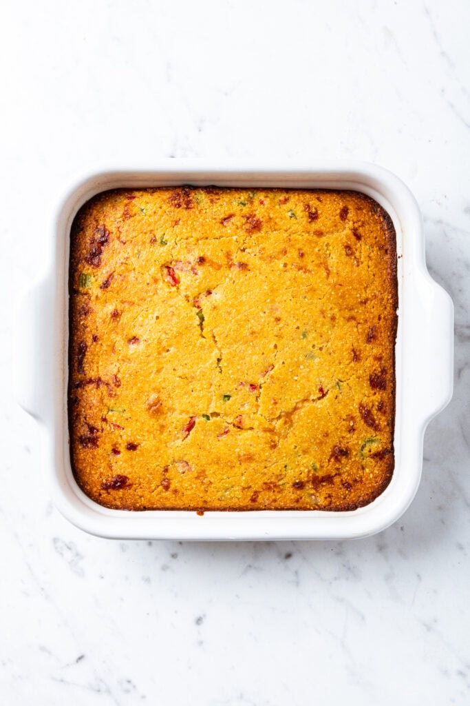 A dish of baked cornbread sits on a marble surface.