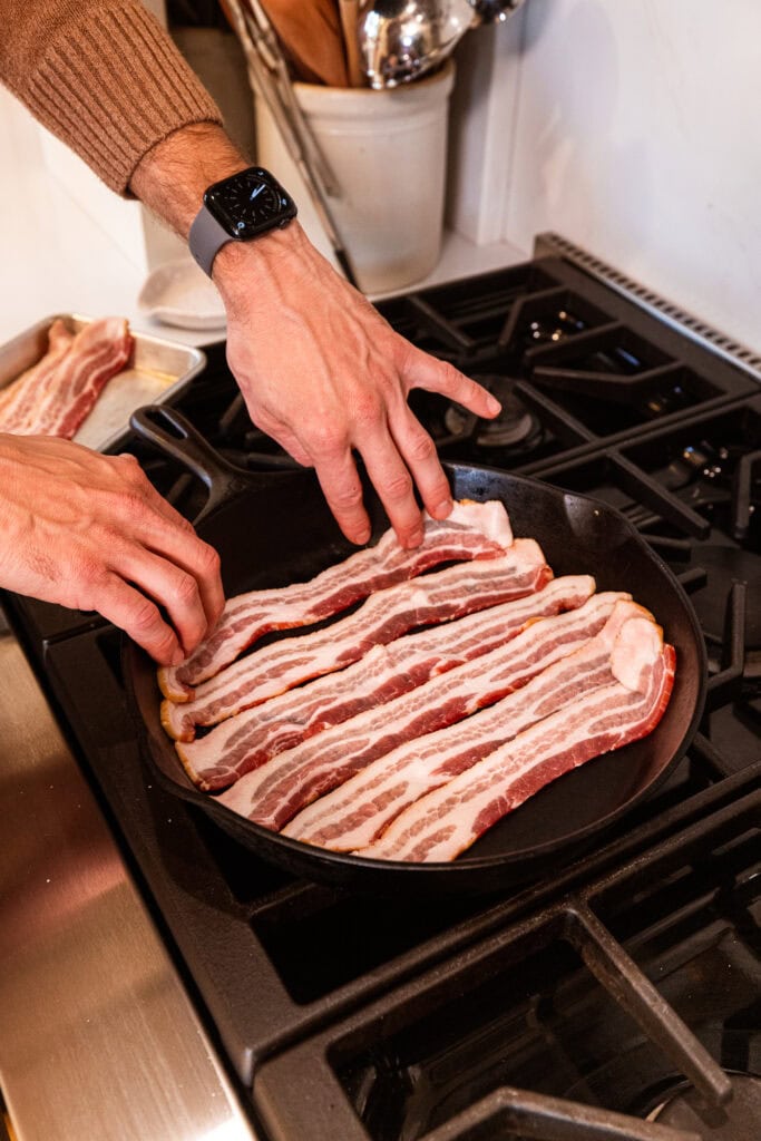 Placing bacon in a skillet to cook.