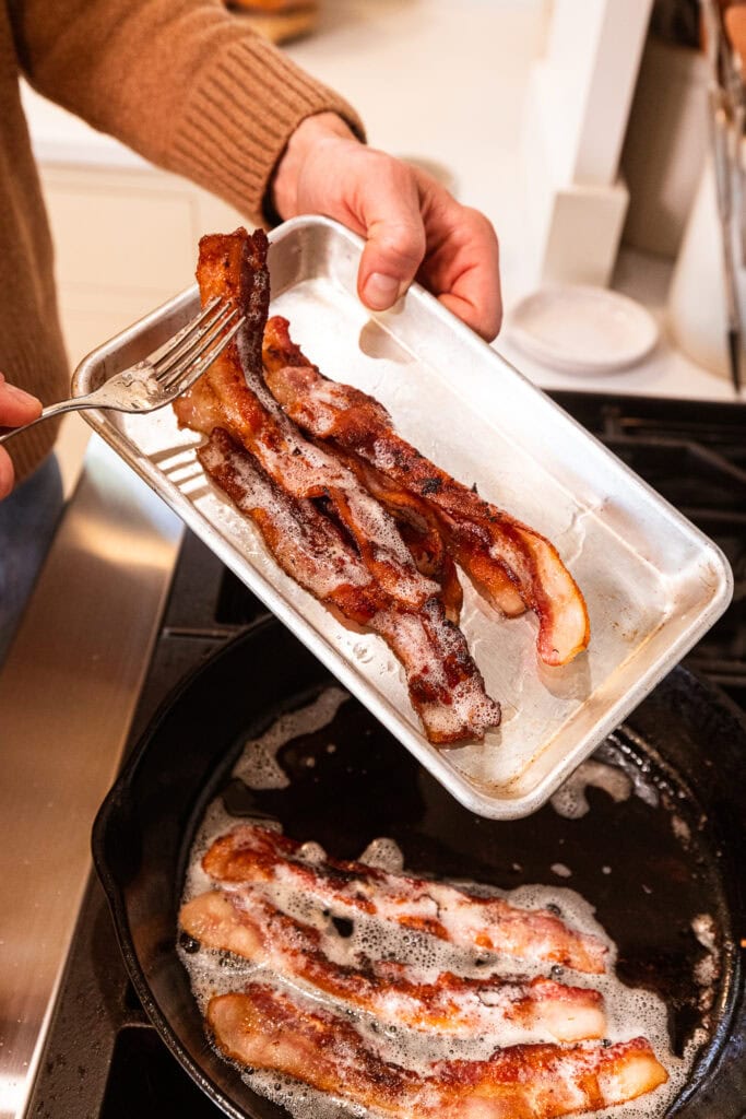 Removing cooked bacon from a skillet.