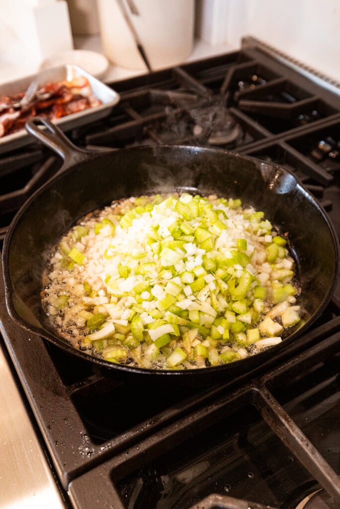 Cooking celery and onion in bacon grease in a skillet.