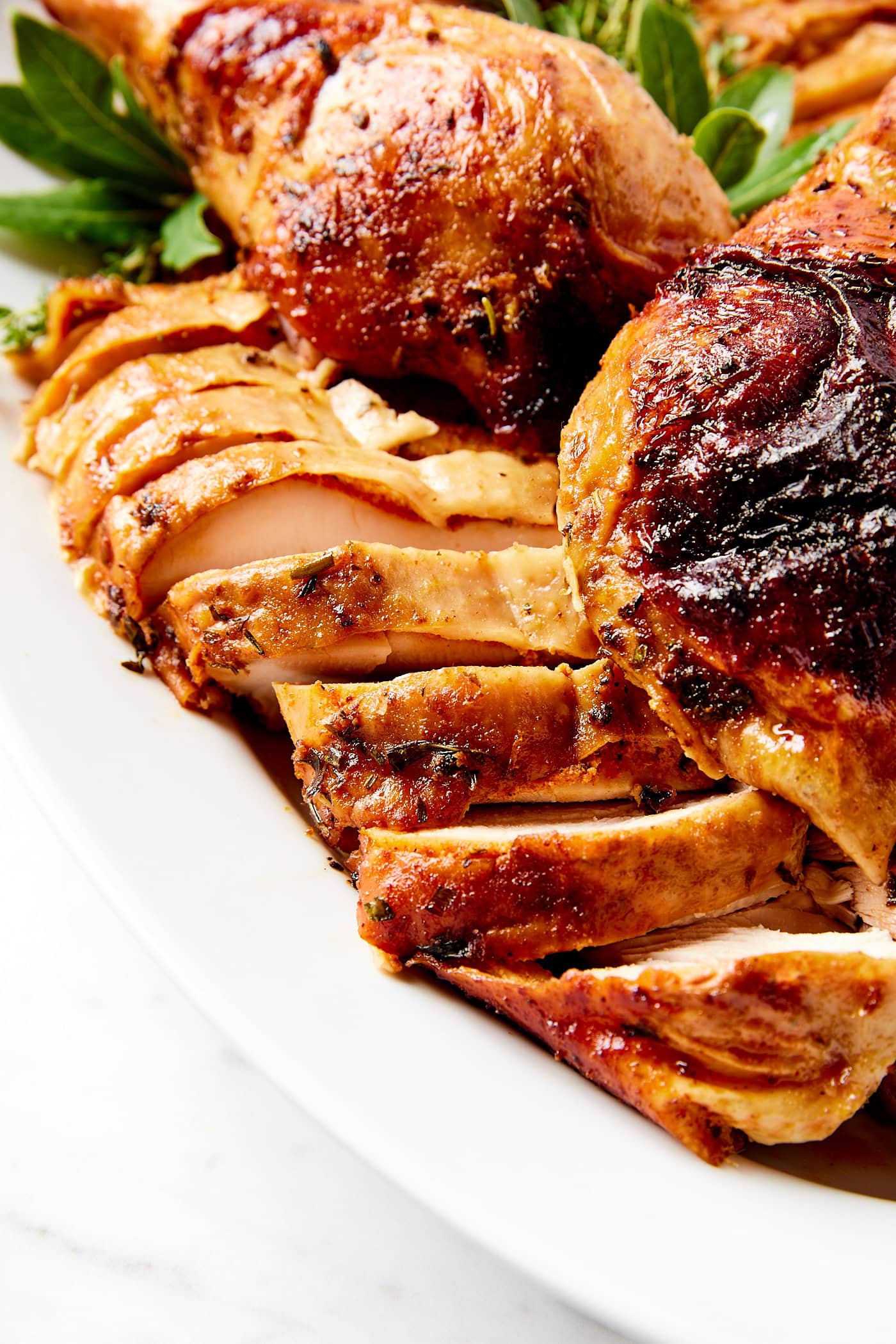 White platter with slices of cowboy butter turkey with crispy skin still attached.