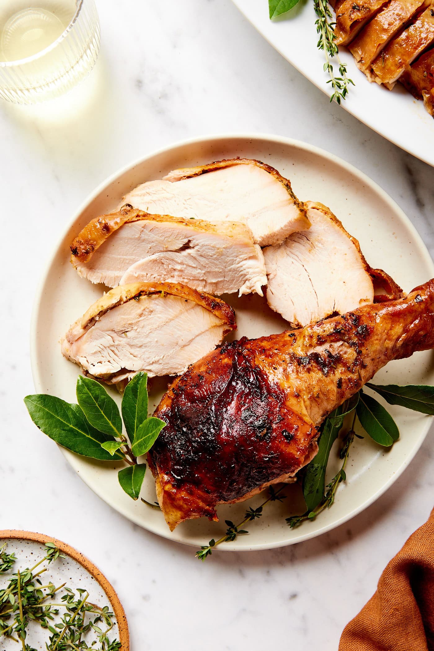 White plate with slices of cowboy butter turkey and a leg with fresh herbs.