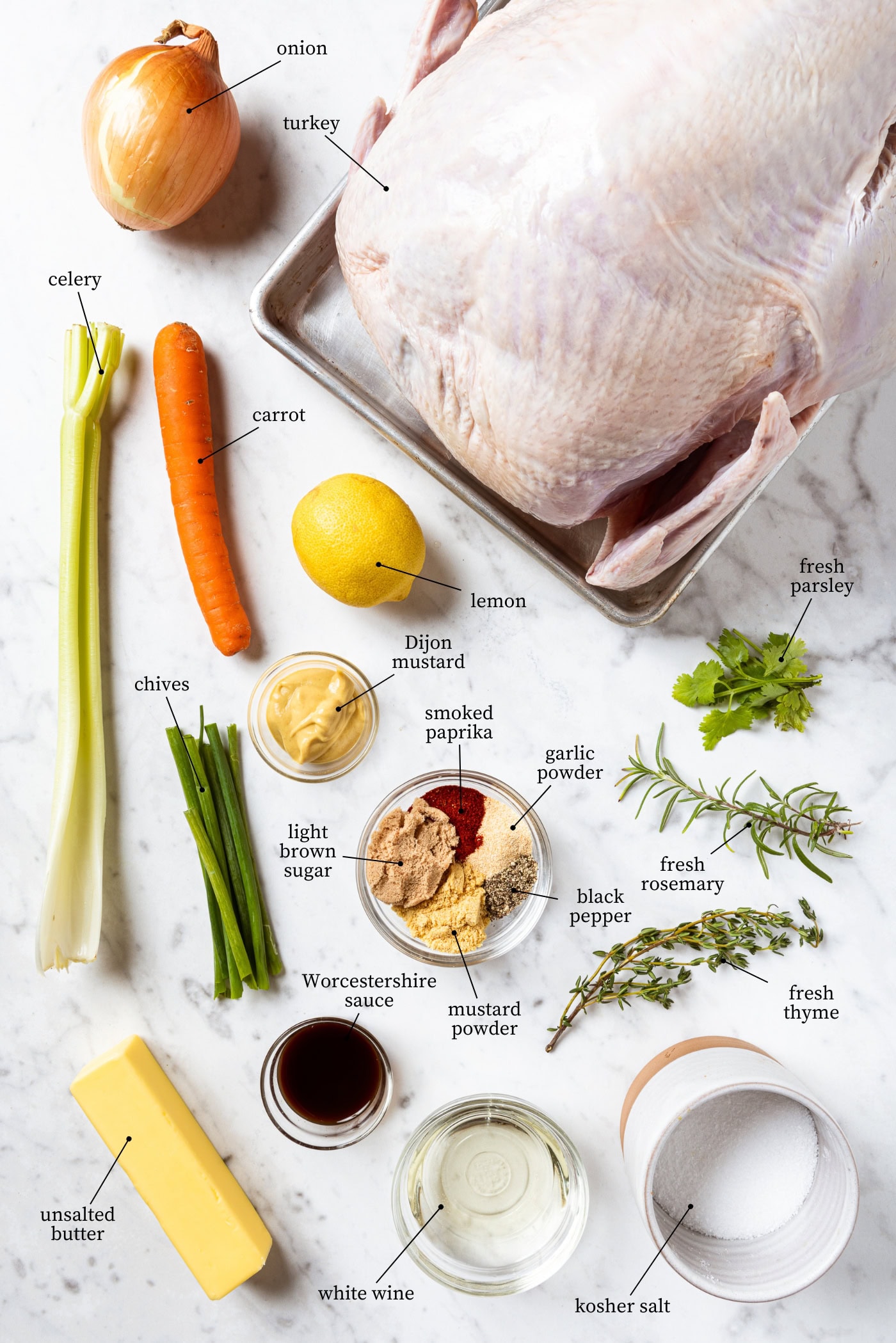 White marble surface filled with ingredients needed for a cowboy butter turkey including spices, herbs, and a raw turkey.