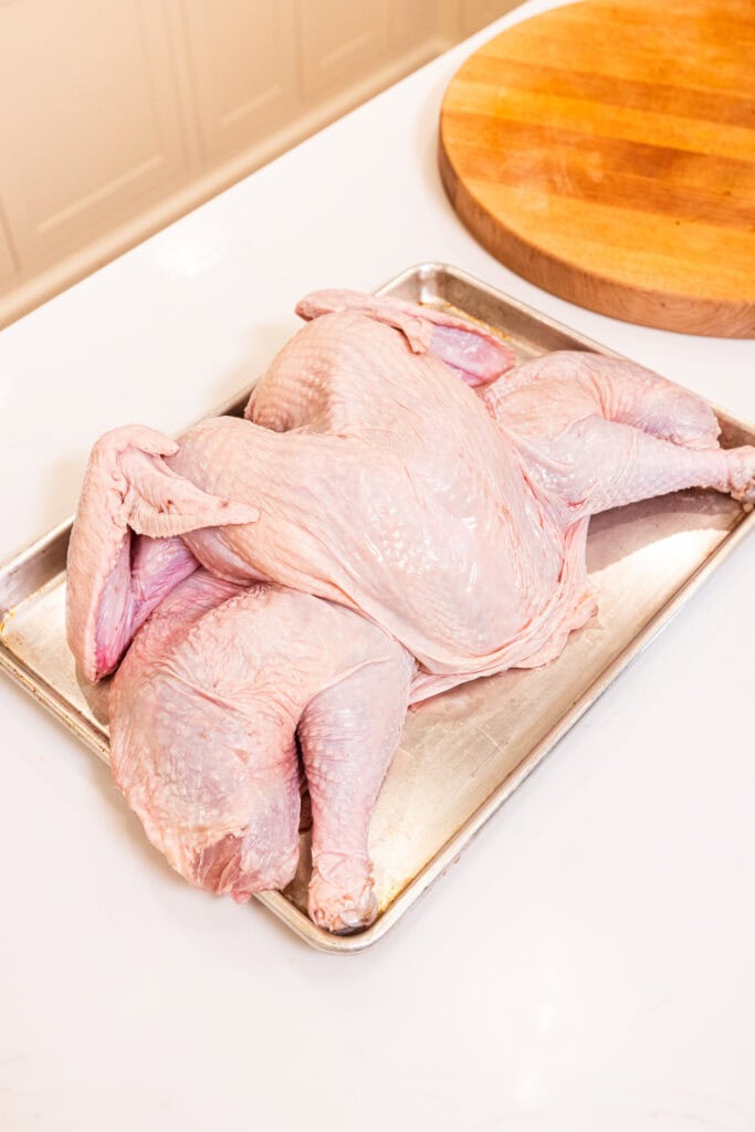 A Thanksgiving turkey sits on a baking sheet prior to cooking.