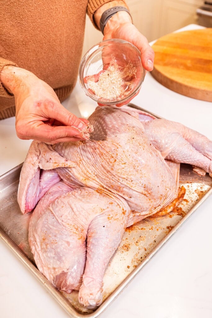 Sprinkling a dry brine over the top of the skin of a cowboy butter turkey prior to cooking.