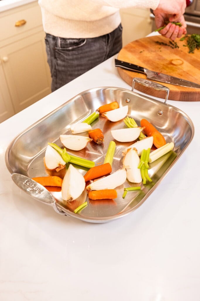 Large pieces of raw vegetables sit in a roasting pan prior to cooking a Thanksgiving turkey.