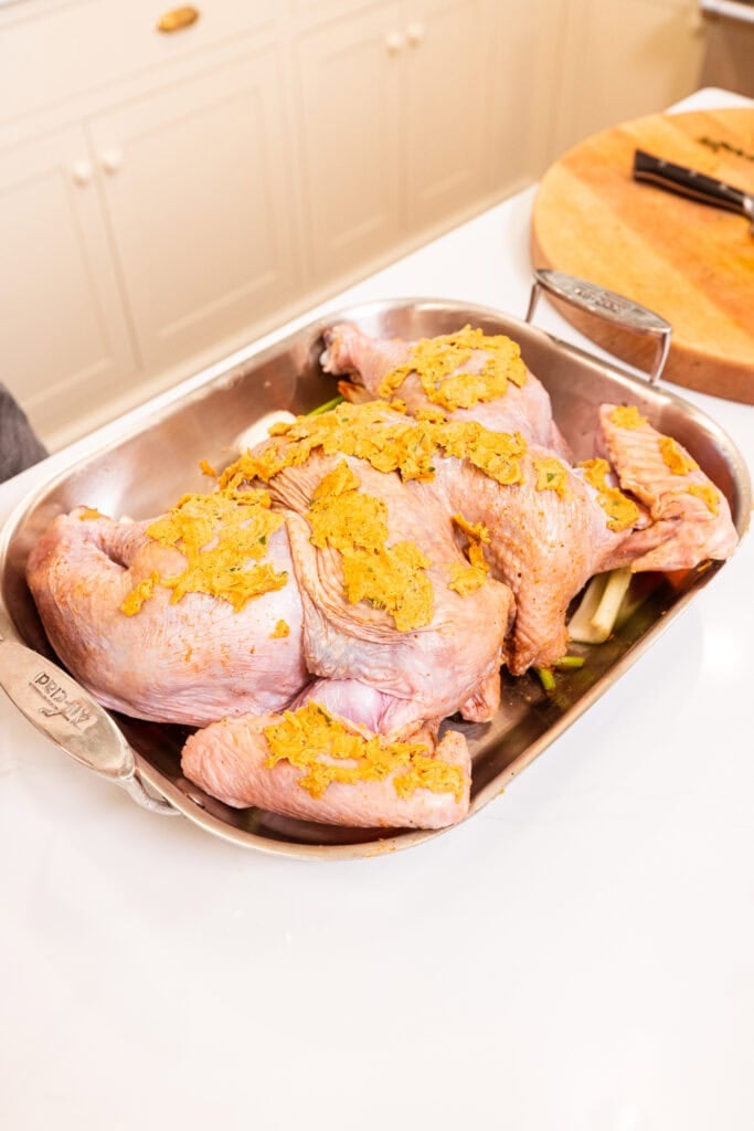 An uncooked turkey covered in a compound cowboy butter sits in a roasting pan.
