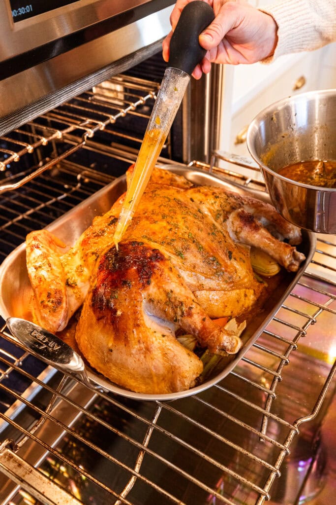 Adding basting liquid to a cowboy butter turkey while it cooks.