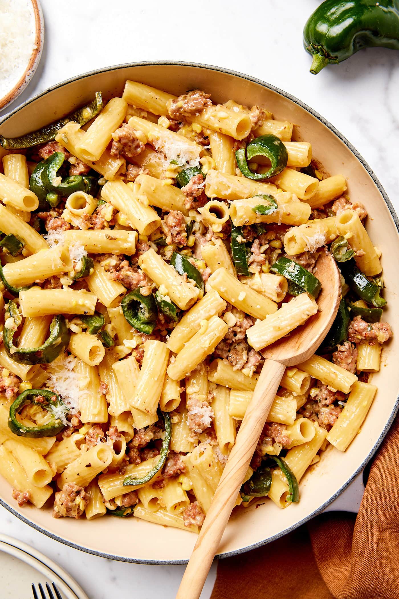 Large bowl filled with sausage pasta with poblano peppers and wooden spoon scooping up a serving.