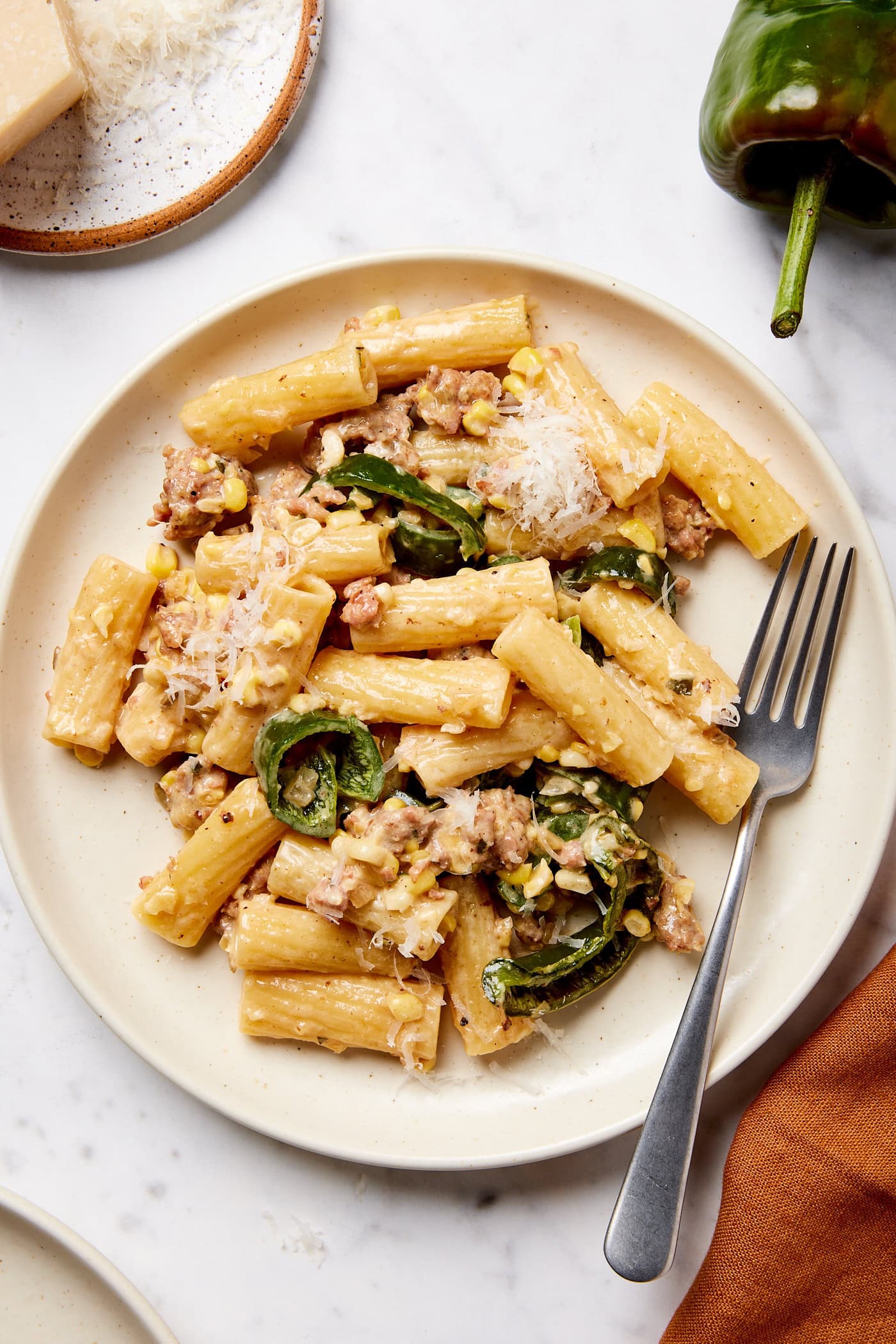 White plate with serving of creamy sausage pasta with a fork resting to the side.