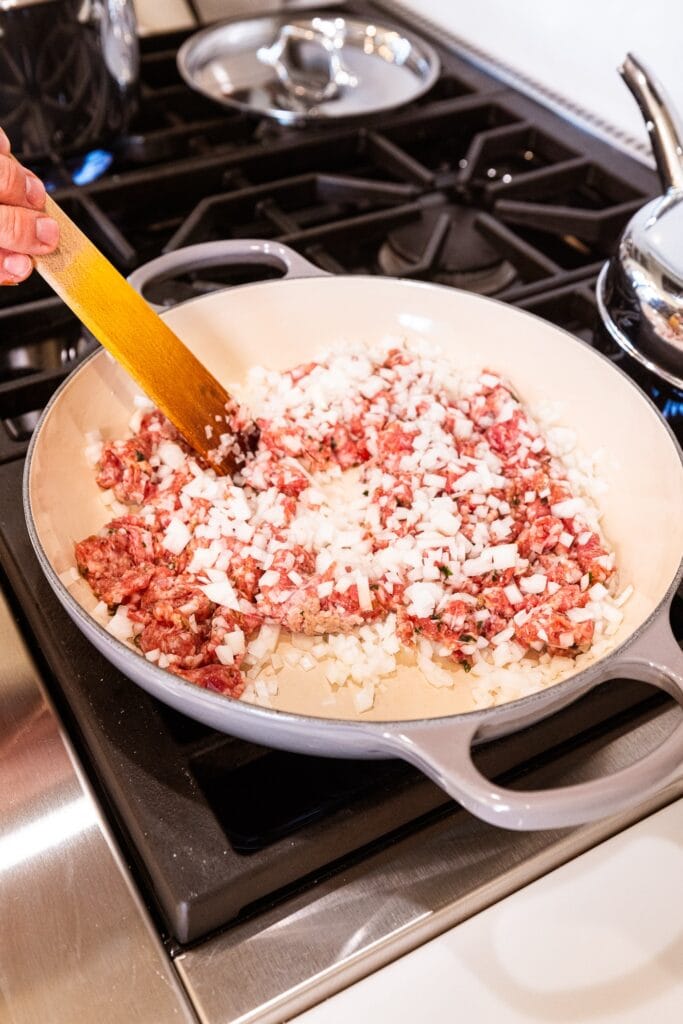 Sausage and onion sit in a skillet beginning to brown.