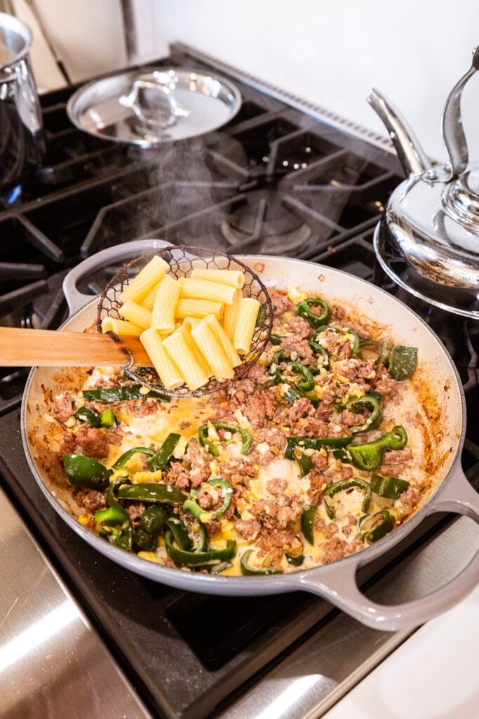Pasta gets added to a skillet with sausage and cream sauce.