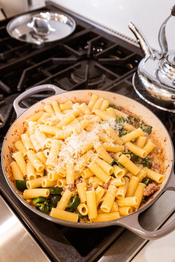 Pasta and grated Parmesan cheese over sausage in a skillet on the stove.