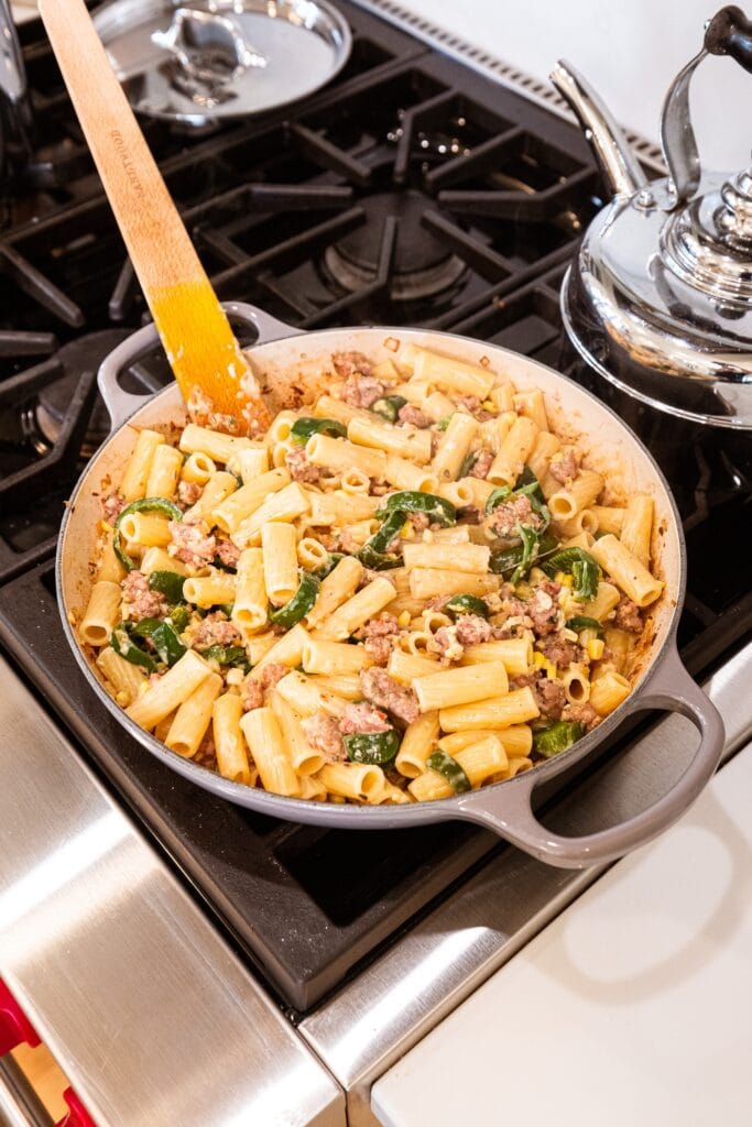 Pasta with sausage and peppers sits in a dish on a stove.