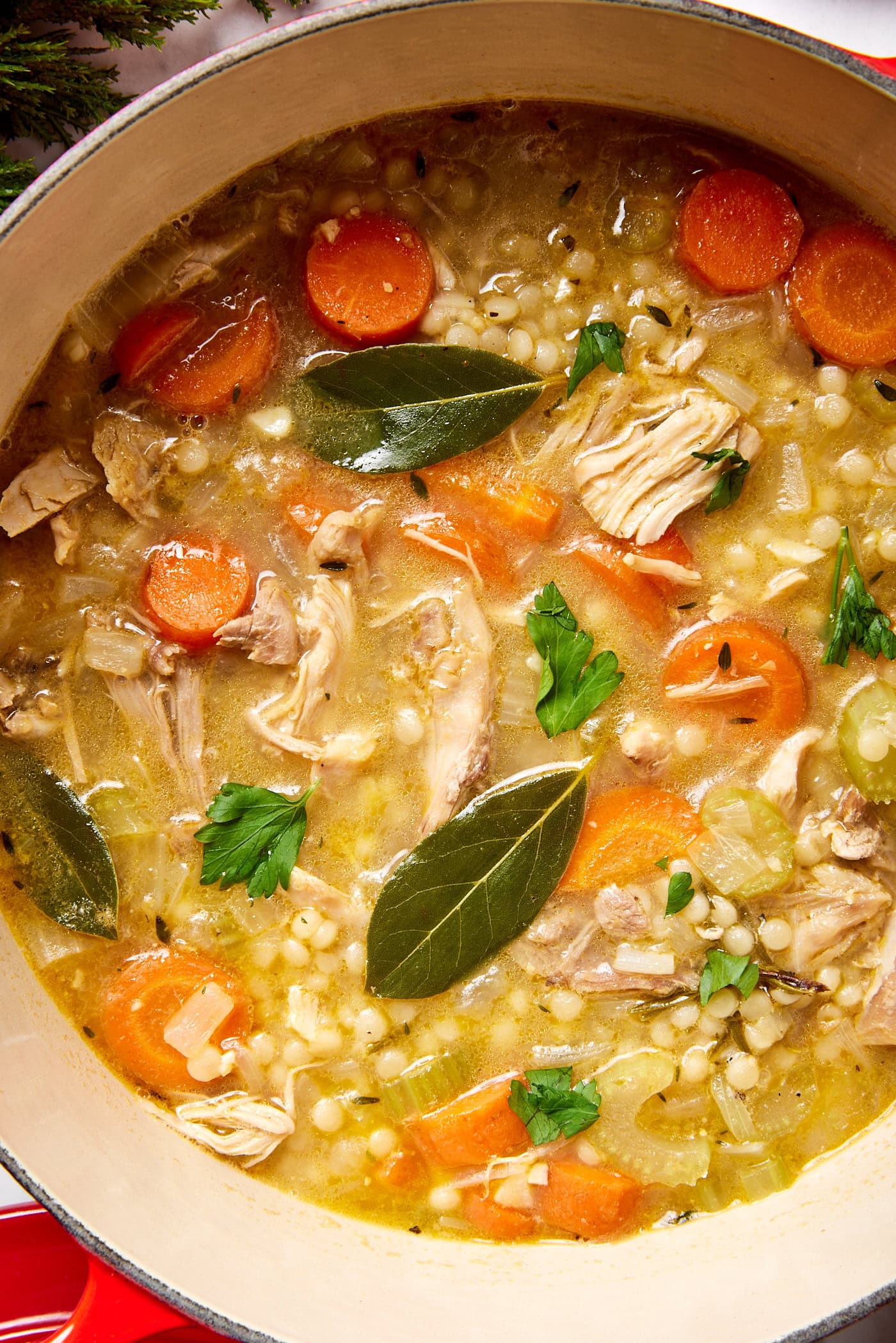 Large stockpot filled with turkey soup with broth-filled soup with pieces of turkey and carrot and bay leaves.