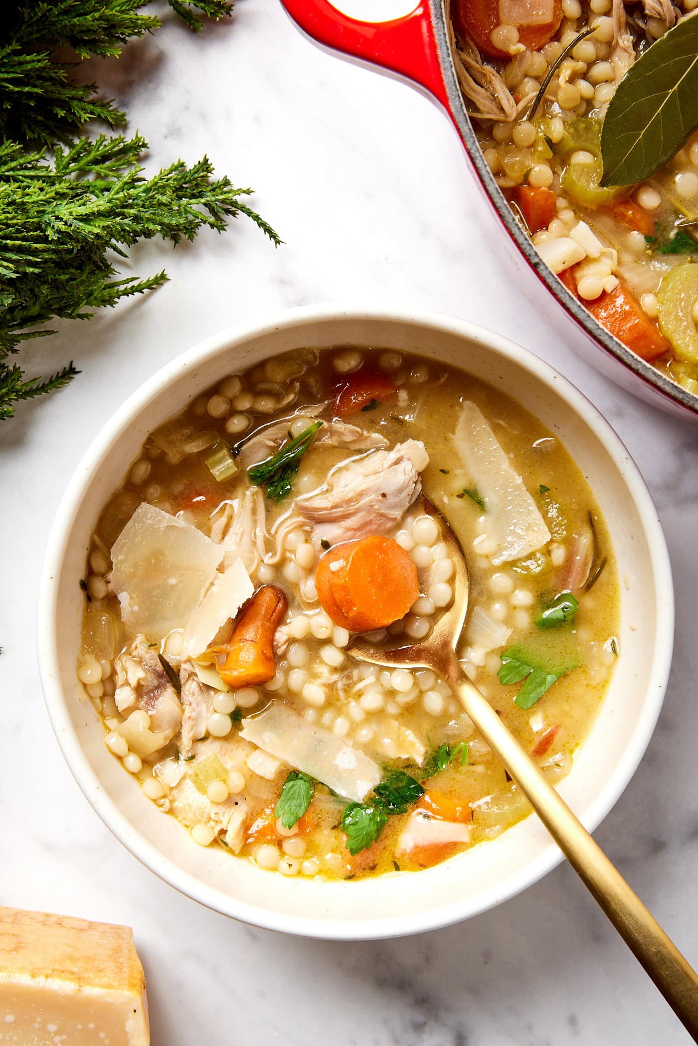 White marble surface with white bowl filled with turkey soup with spoon scooping up a bite.