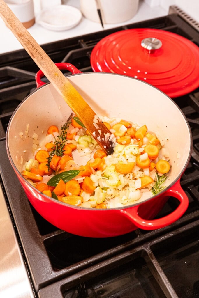 Carrot, onion, and celery cook in a pot with herbs.