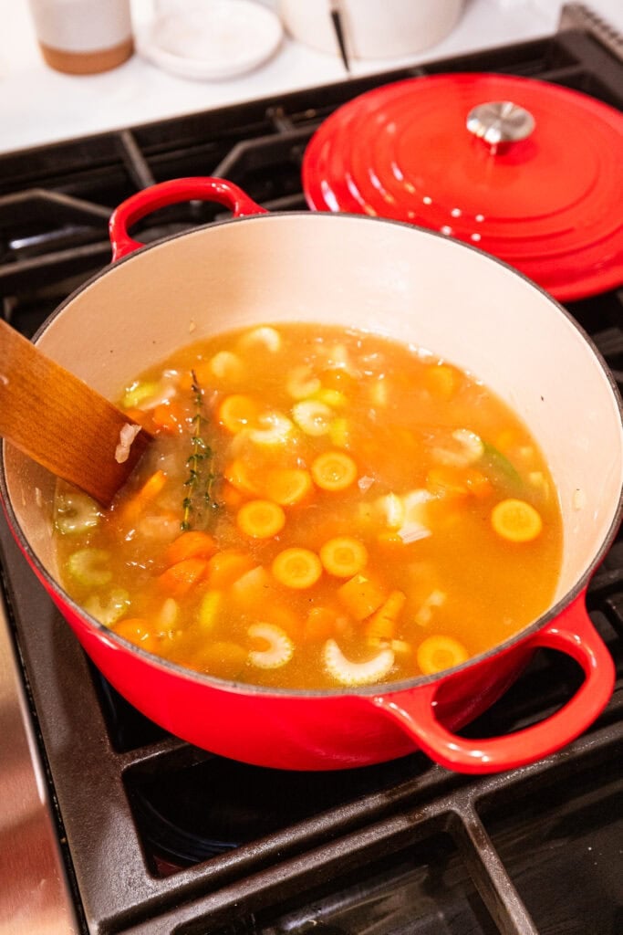 Carrot, celery, and onion cook with turkey stock in a pot on a stove.