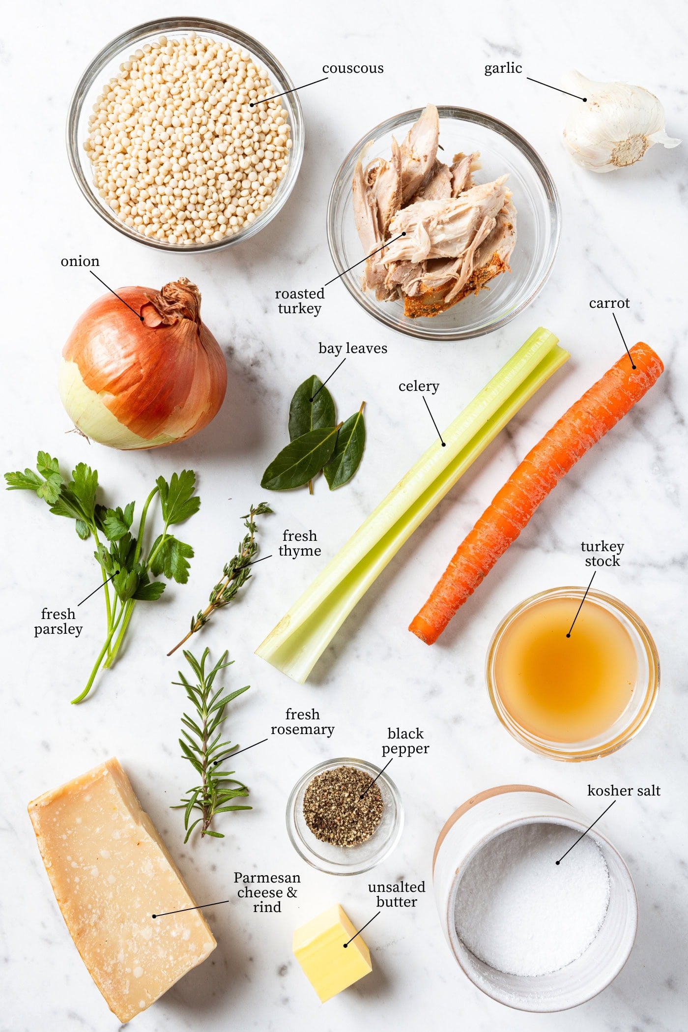 White marble surface filled with ingredients needed for leftover turkey soup including turkey, couscous, celery, carrot, and more.