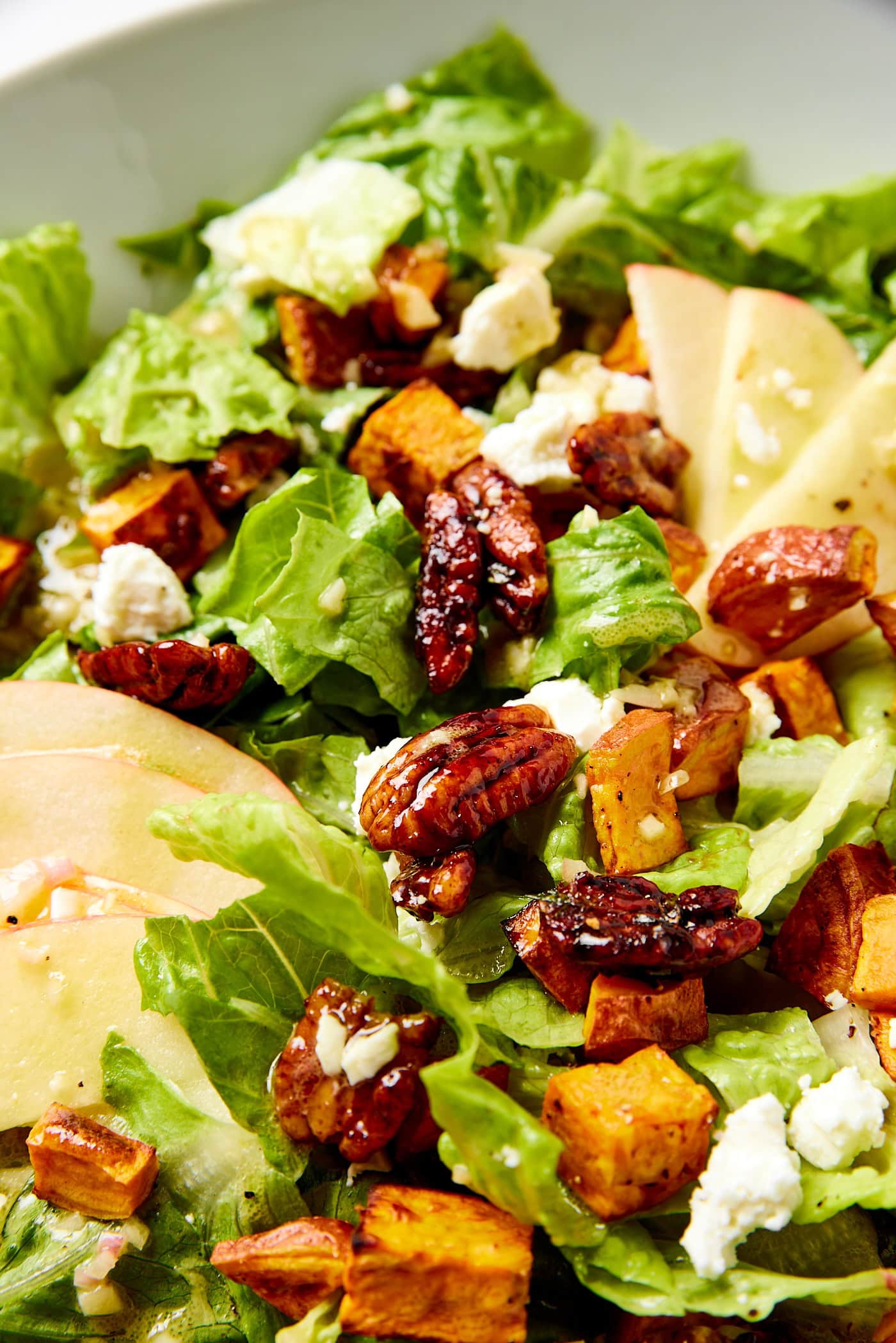 Candied pecans and pieces of roasted sweet potato sitting on lettuce with crisp apple to the side.