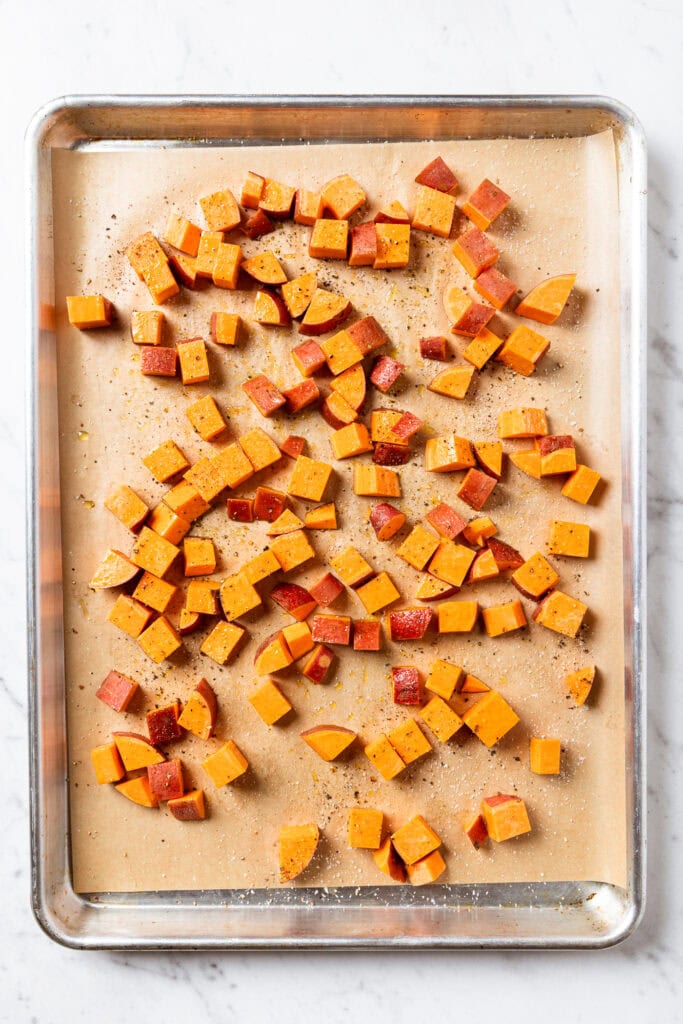 Raw pieces of sweet potato on a parchment-lined baking sheet prior to roasting.