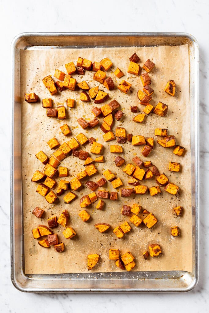 Pieces of roasted sweet potato on a parchment-lined baking sheet.