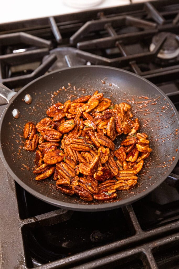Pecans roast in a pan over a stove.