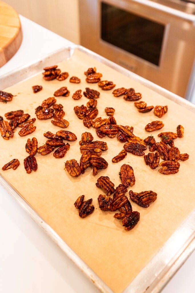 Roasted pecans cool on a parchment-lined baking sheet.