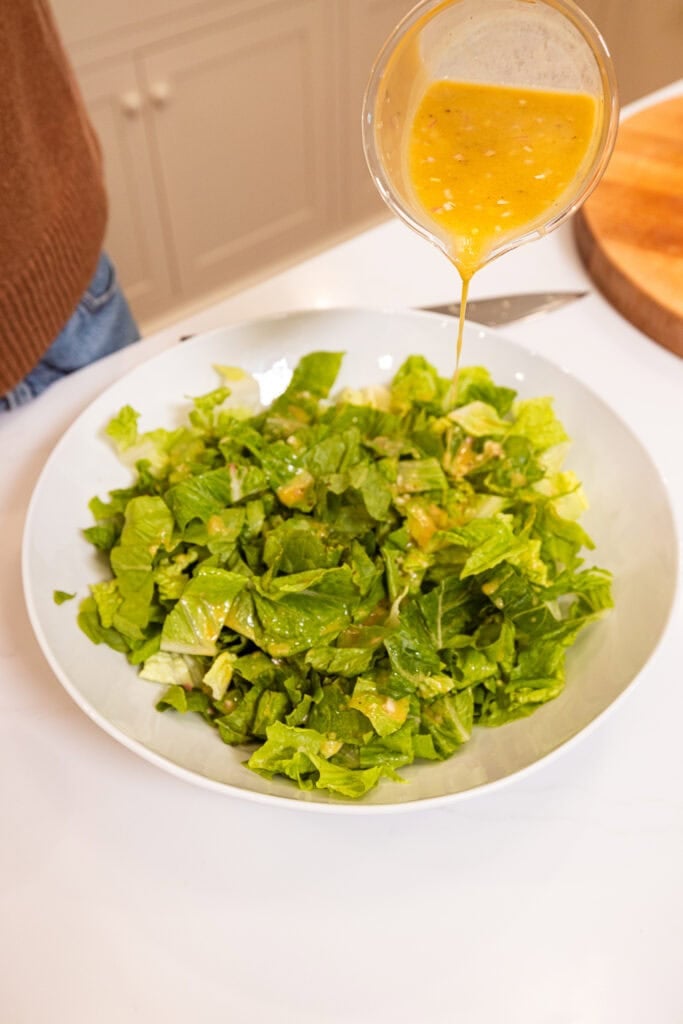 Vinaigrette getting drizzled over lettuce.