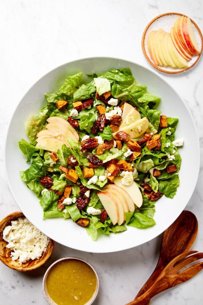 White bowl with sweet potato salad with apples, pecans, and feta and drizzled with salad dressing.