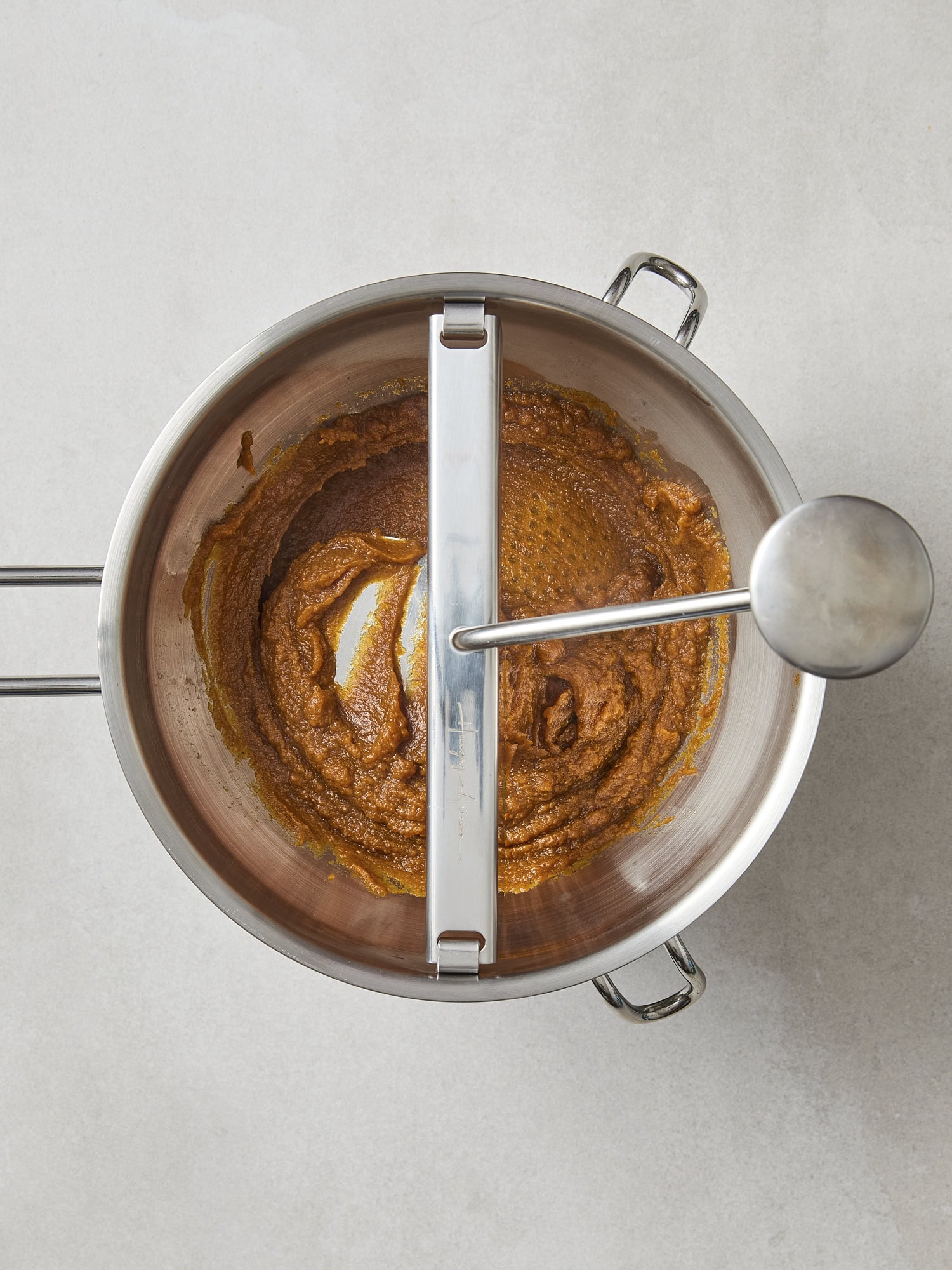 Food mill breaking down cooked pumpkin butter into finer texture.
