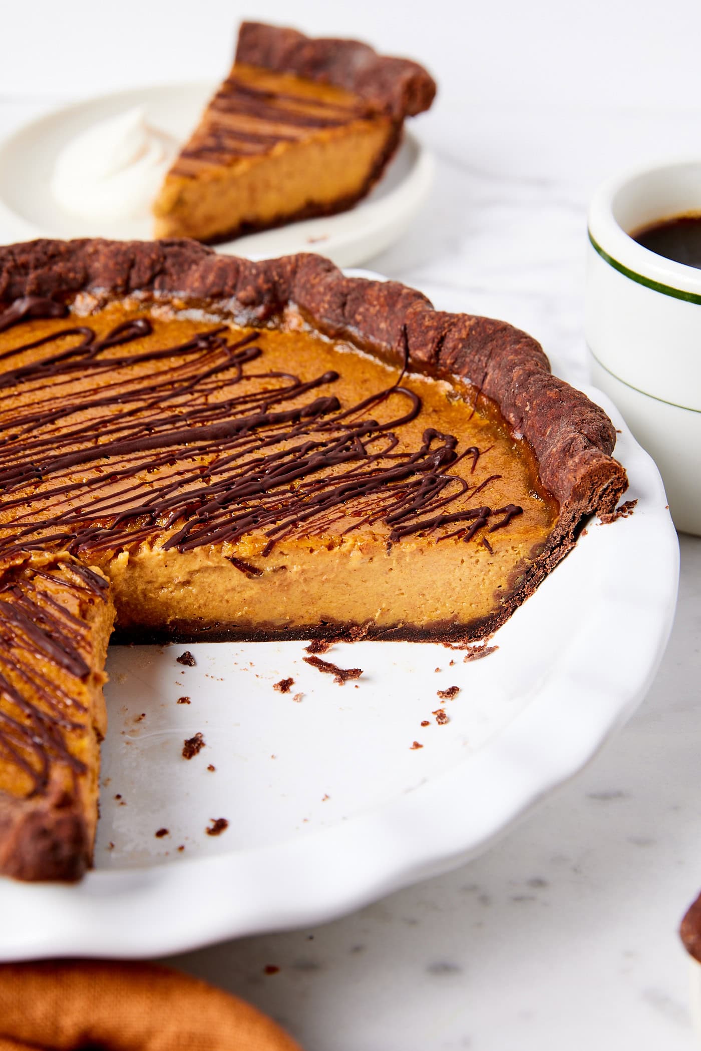 White pie plate with pumpkin pie made with a chocolate crust with chocolate drizzled on top.