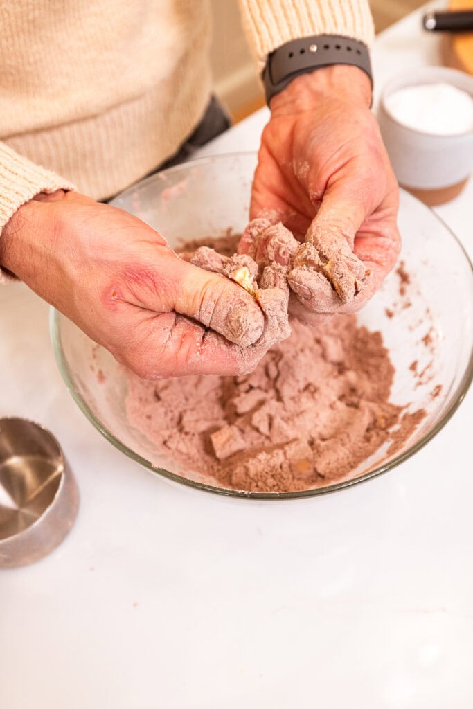 Using thumbs and forefingers to press cubes of butter into dry ingredients.