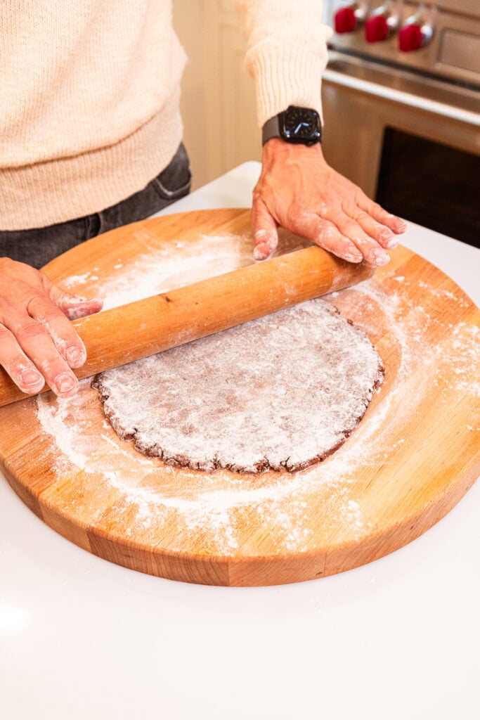 Rolling out a disk of chocolate pie dough on a floured cutting board.