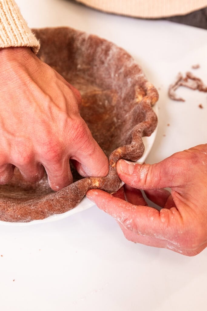 Crimping the edge of the pie crust in the dish.