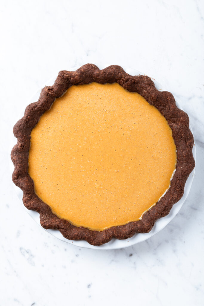 Pumpkin pie with a chocolate crust in a pie dish prior to baking.