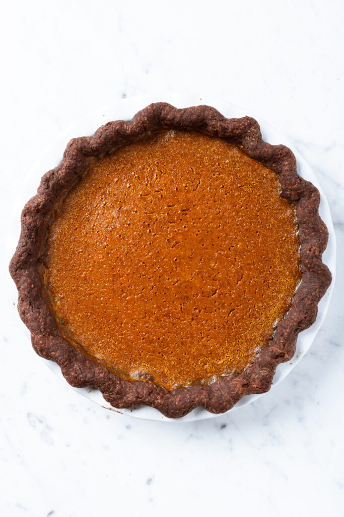 A baked pumpkin pie with chocolate crust sits on a counter.