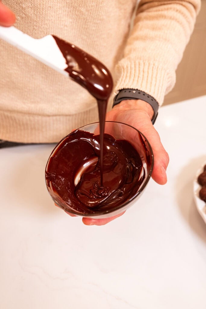 Hand holding bowl filled with melted chocolate for drizzling.