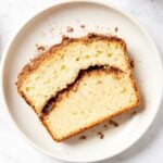 White plate on marble surface with slice of coffee cake with cinnamon in the center.